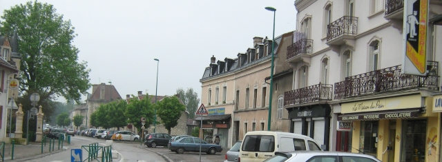 a french street with a few shops and the boulangerie in the rain looking grey and miserable 